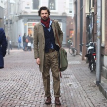 Patterned jacket, rolled cuffs on his pants, a cardigan, a man purse, a scarf