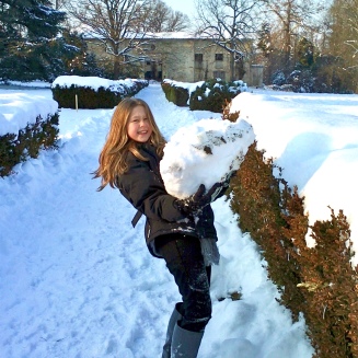 a young girl holding an enormous snow ball.