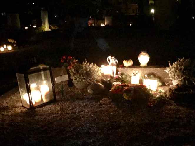 a grave with lighted candles, lanterns and trinkets